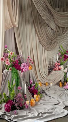 an arrangement of flowers and candles are on the floor in front of draping