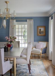 a dining room with blue walls, white chairs and a chandelier hanging from the ceiling