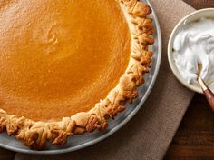 a pumpkin pie sitting on top of a table next to a bowl of whipped cream