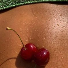 two cherries sitting on the side of a woman's stomach with water droplets all over them