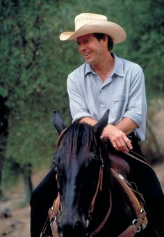 a man riding on the back of a black horse wearing a cowboy's hat