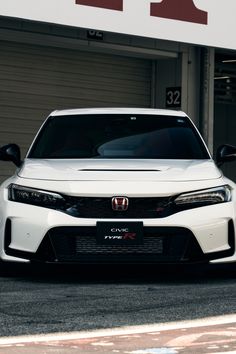 the front end of a white car parked in front of a garage with an awning