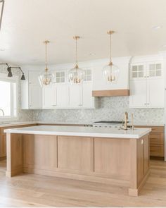 an empty kitchen with white cabinets and wood flooring is pictured in this image, there are three pendant lights hanging from the ceiling