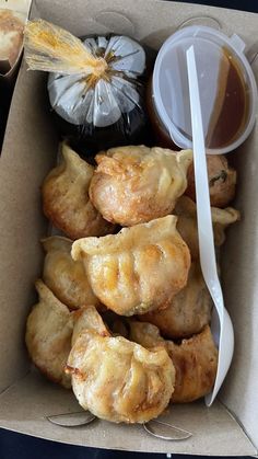 a box filled with different types of pastries next to a cup of sauce and spoon