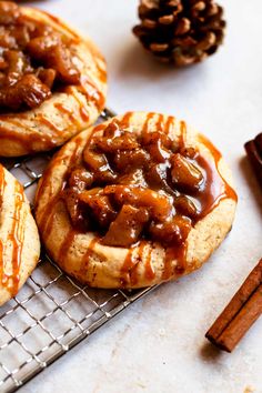 three cookies with caramel toppings on a cooling rack next to some cinnamon sticks