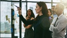 a group of people standing in front of a glass wall with sticky notes on it