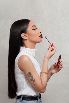 a woman with long black hair is holding a lipstick in one hand and looking at the other