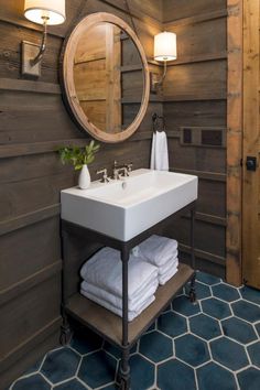 a bathroom with wooden walls and blue tile flooring, along with a round mirror on the wall