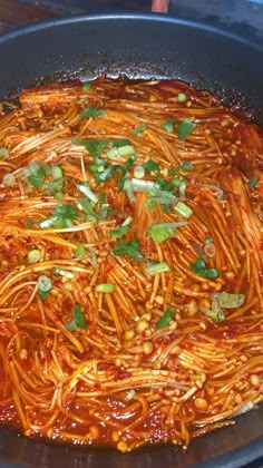 a pan filled with spaghetti and garnishes on top of a wooden table