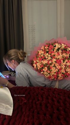 a woman laying in bed with a large bouquet of flowers on her head and another person holding a cell phone