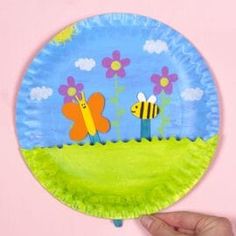 a paper plate that has some flowers and bees on it with a blue sky in the background