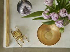 a marble tray topped with a vase filled with flowers and a gold spider figurine