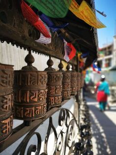 many bells are hanging on the side of a building with people walking by in the background