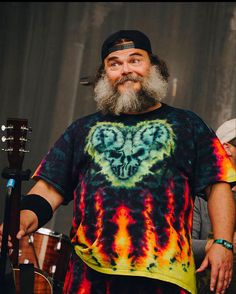 a man with a beard wearing a tie - dyed shirt and holding a guitar in his hand