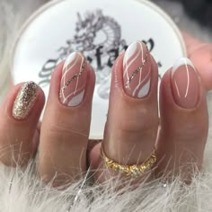 a woman's hands with white and gold manies on their nails, in front of a feathery background