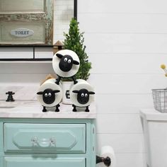 three black and white sheep sitting on top of a bathroom counter next to a toilet