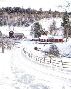 a snow covered country road with houses on the side and trees in the background,