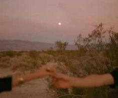 two people reaching out their hands to touch each other in the desert at night time