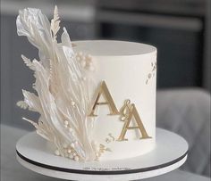 a white wedding cake with gold letters and flowers on the top is sitting on a plate