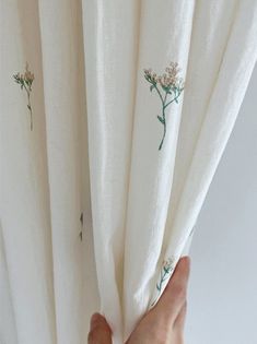 a hand is holding the curtains with flowers drawn on them, and they are open