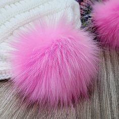 two pink pom - poms on top of a white knitted hat sitting on a wooden floor