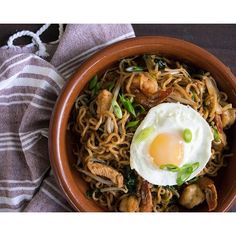 a brown bowl filled with noodles, meat and an egg on top next to a striped towel