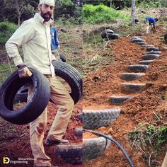 a man is holding two tires and standing in front of some dirt with another person behind him