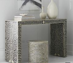 a black and white console table with two vases on top of it, next to a small stool