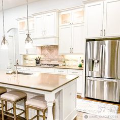 a large kitchen with white cabinets and stainless steel appliances in the center, along with two bar stools