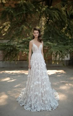 a woman in a white wedding dress standing on the street with trees behind her and looking at the camera