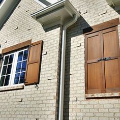 two wooden shutters on the side of a brick building with white trim and windows