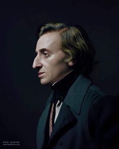 a man with long hair wearing a black suit and tie, looking off to the side