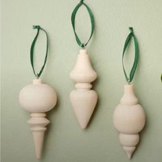 three white ornaments hanging on the wall with green ribbon around them and one is shaped like a cone