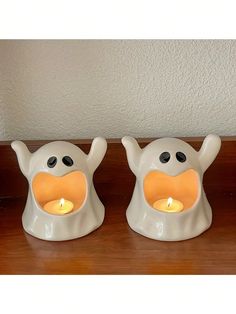 two white ceramic candlesticks with black eyes and nose on top of a wooden table