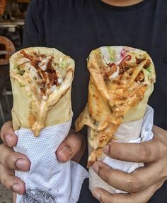 two people holding up some tacos with meat and vegetables on them in their hands