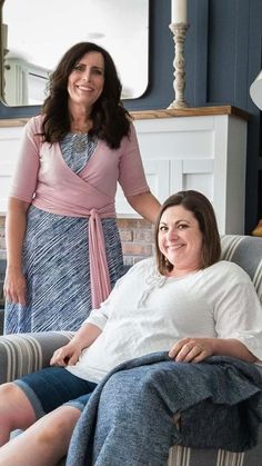 two women are sitting on a couch smiling and posing for the camera while one woman stands behind them