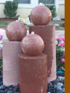 a statue made out of concrete sitting in the middle of some rocks and flowers near a house