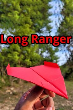 a hand holding a red paper airplane with the words long ranger on it and trees in the background