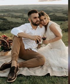 a man and woman sitting on top of a blanket next to each other holding wine glasses