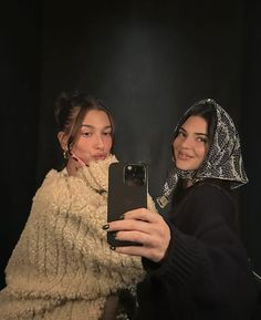 two women taking a selfie in front of a black background with their cell phones