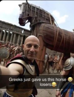 a man standing in front of a horse statue next to another man wearing roman armor