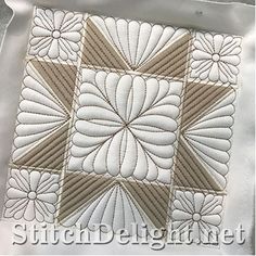 a white and brown quilted square with flowers on the center, in front of a silver background