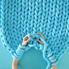 a person is holding up a blue knitted object with their hands and fingers on it