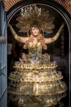 a woman is dressed in gold and surrounded by wine glasses