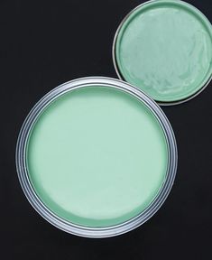 two tins with green paint sitting on top of a black tableclothed surface