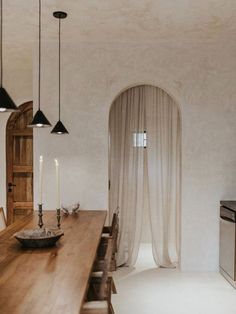 a dining room table with chairs and lights hanging from it's ceiling, in front of an arched doorway