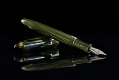 a green fountain pen sitting on top of a black table next to another pen and its reflection