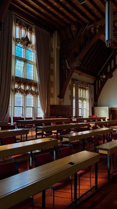 rows of tables and chairs in a large room with stained glass windows on the wall