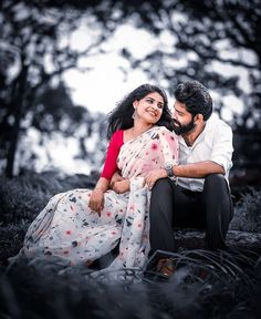 a man and woman sitting next to each other on the ground in front of trees