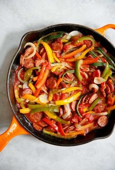 a skillet filled with vegetables sitting on top of a white tablecloth next to an orange spatula